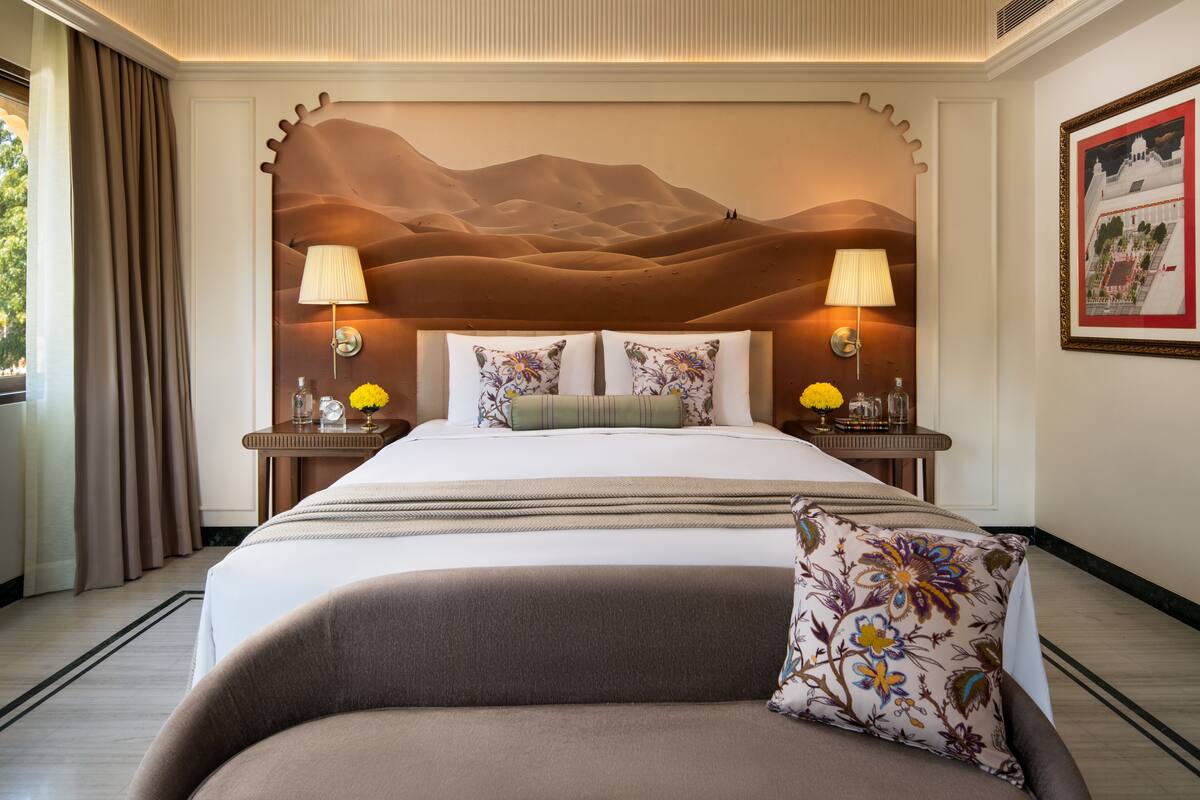 Une chambre d’hôtel avec un grand lit, deux tables de chevet avec des lampes, une fresque murale décorative et un tableau encadré au mur.