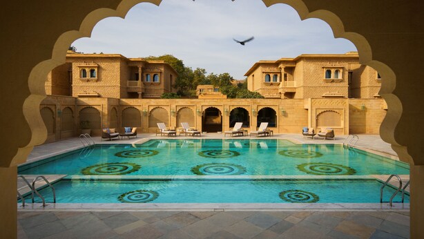 A swimming pool with a geometric pattern, surrounded by lounge chairs and a traditional building with arched windows and balconies. - Taj Gorbandh Palace, Jaisalmer (Jaisalmer)