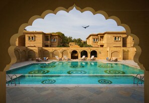 A swimming pool with a geometric pattern, surrounded by lounge chairs and a traditional building with arched windows and balconies. - Taj Gorbandh Palace, Jaisalmer (Jaisalmer)