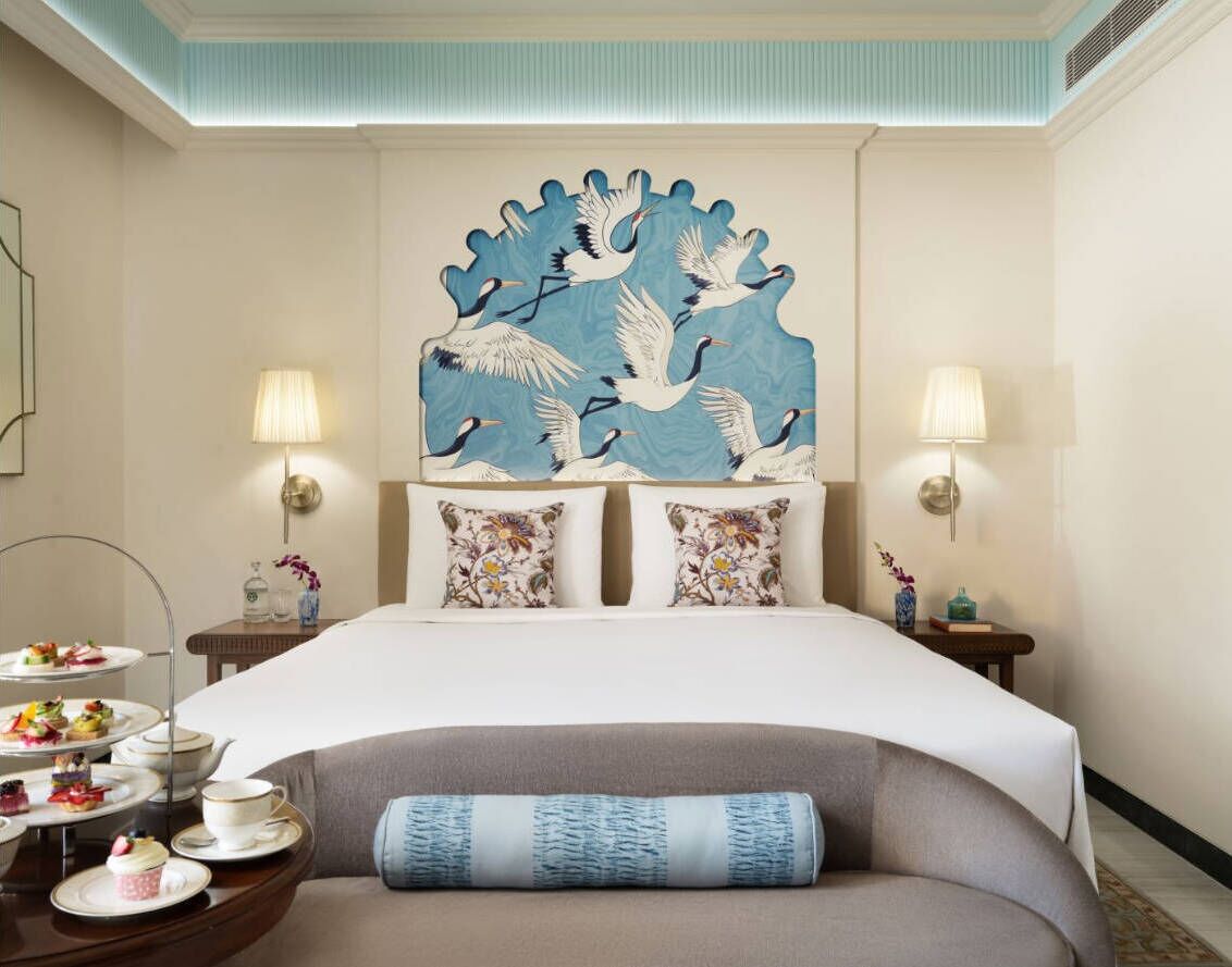 Une chambre d’hôtel comprenant un lit, deux tables de chevet, un élément décoratif mural et une petite table avec un service à thé.