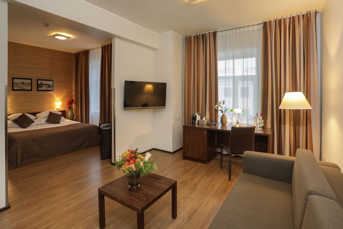 Een hotelkamer met een bed, een bureau, een televisie, een bank en een bijzettafeltje met bloemen.
