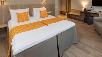 A hotel room with a double bed, two pillows, a bedside table, a chair, a desk, and a TV.