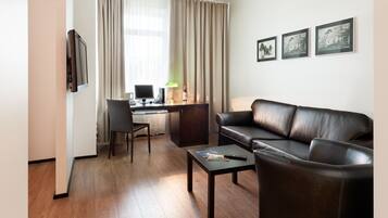 Een moderne hotelkamer met een leren bank, een bureau met computer, een stoel en een flatscreen televisie.