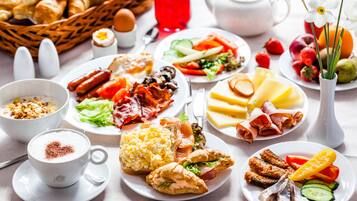 Un bufé de desayuno con diversos platos, entre ellos huevos, carnes y frutas.
