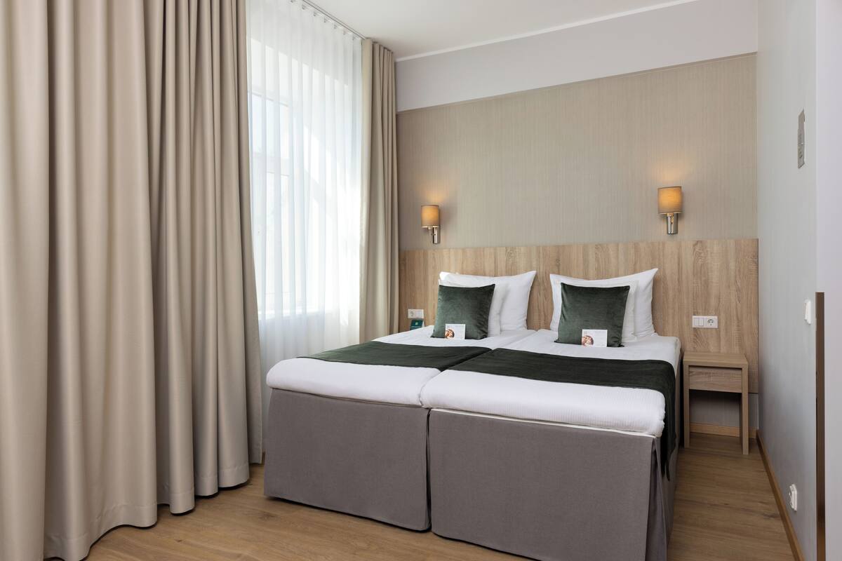 Ein Hotelzimmer mit einem großen Bett, zwei Nachttischlampen, einem hölzernen Kopfteil und einem fenster mit Vorhängen.