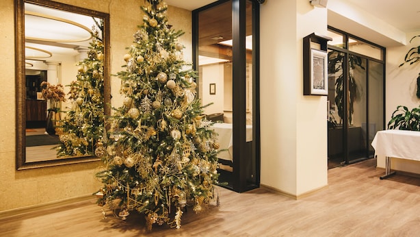 A Christmas tree in a hotel lobby with a mirror and a table with a white tablecloth. - Kreutzwald Hotel Tallinn (Tallinn)
