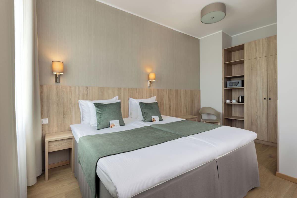 Ein ordentlich eingerichtetes Hotelzimmer mit einem großen Bett, zwei Nachttischen, einem Sessel, einem Kleiderschrank und zwei Wandlampen.