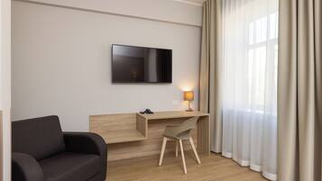 A modern hotel room with a wooden desk, a flat-screen TV, a sofa, and a lamp.