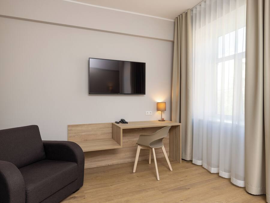 Moderni hotellihuone, jossa on puinen työpöytä, litteänäyttöinen televisio, sohva ja lamppu.