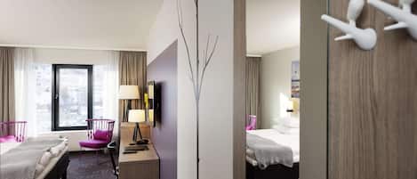 A hotel room with two beds, a desk, a chair, a mirror, and a view of the city.