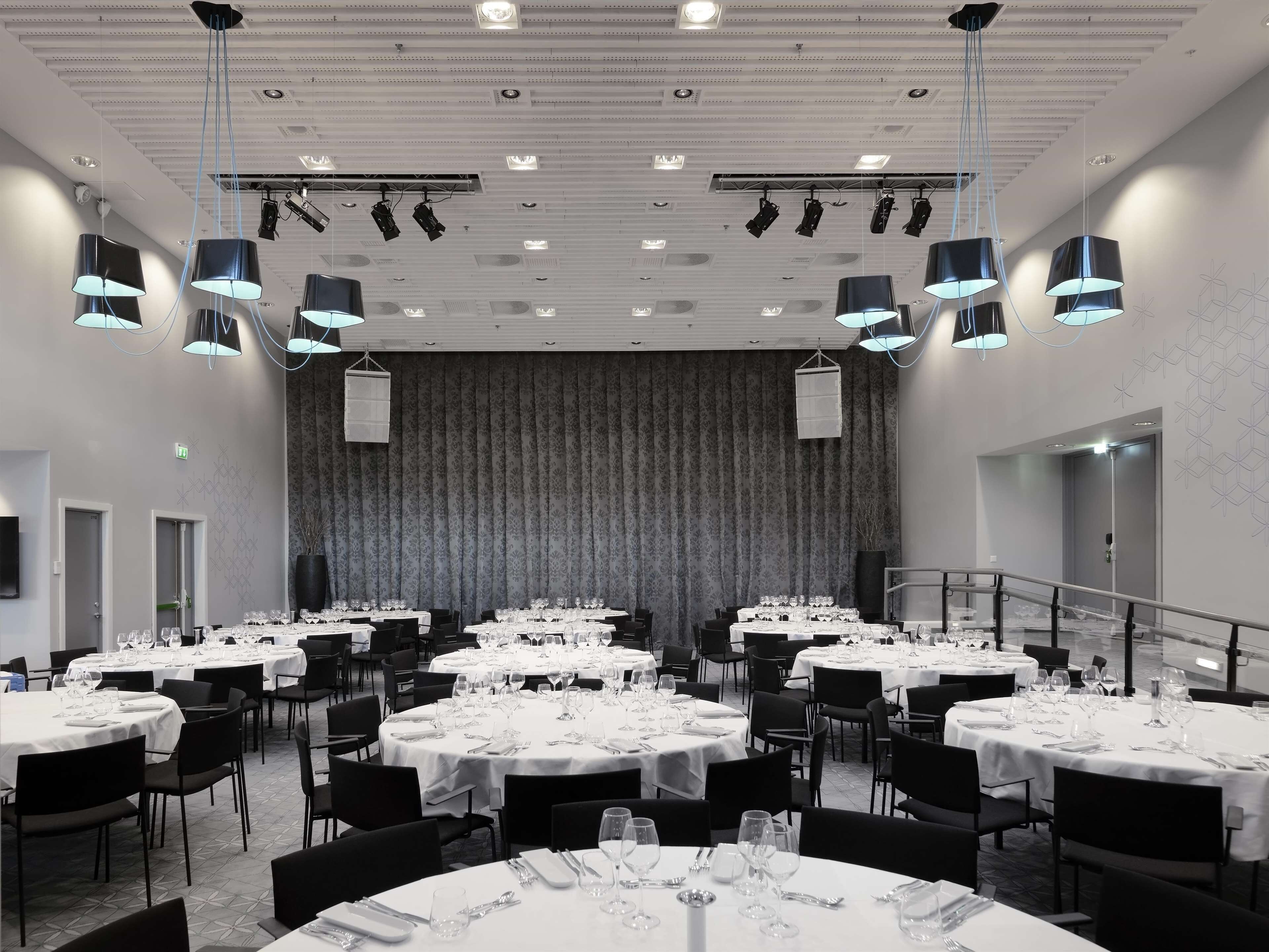 Un amplio salón de banquetes con varias mesas redondas dispuestas para el servicio de comidas, equipado con sillas y vajilla.