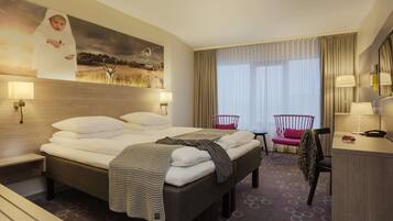 A hotel room with a large bed, a desk, a chair, a small table, and a window with curtains.