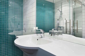 A modern bathroom with a white sink, a glass shower enclosure, and teal-tiled walls.