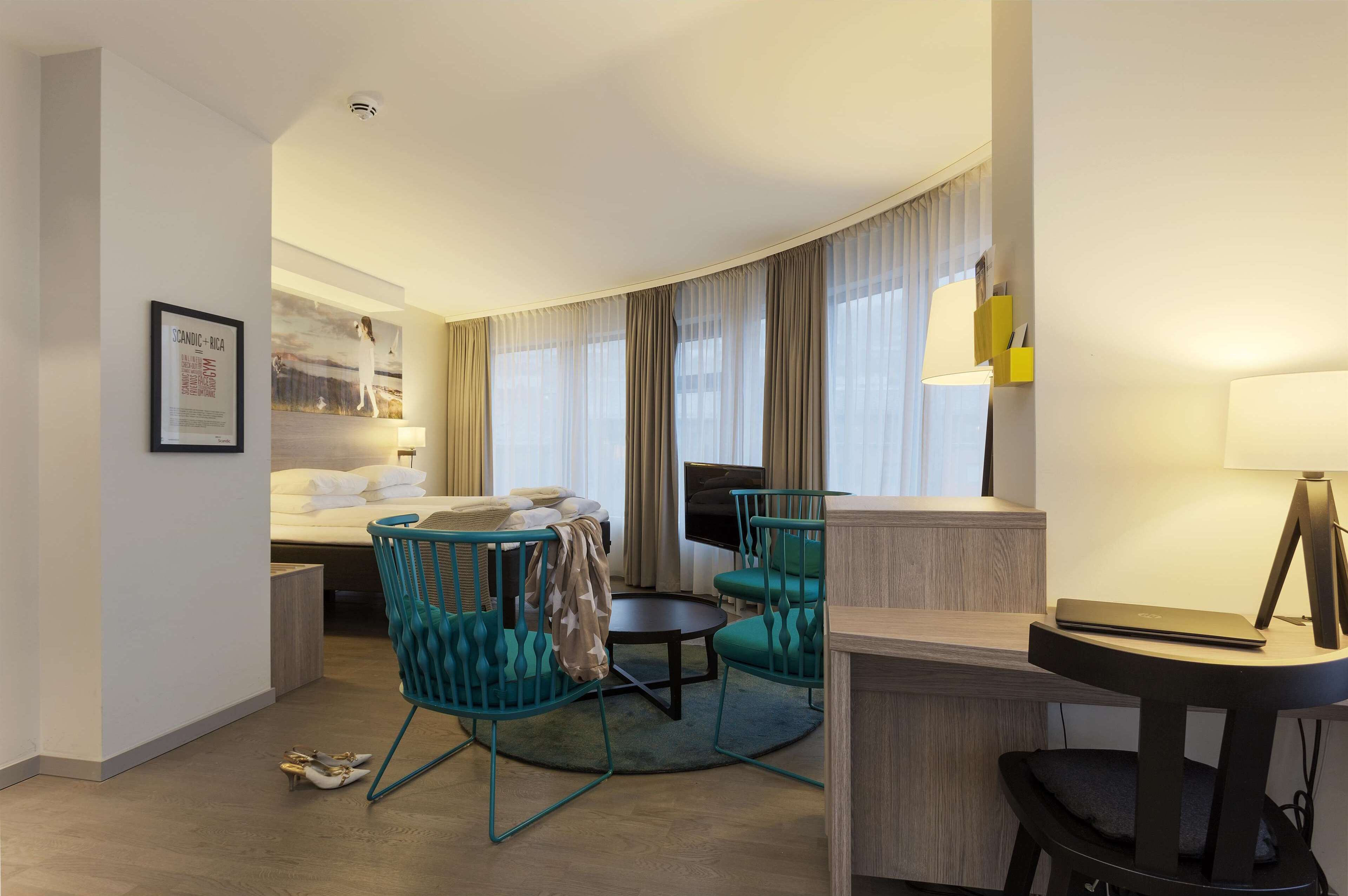 Une chambre d’hôtel avec un lit, deux chaises, un bureau, une télévision et une lampe.