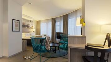 A hotel room with a bed, two chairs, a desk, a TV, and a lamp.