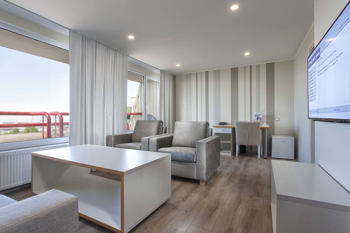 Une chambre d’hôtel moderne dotée d’une grande fenêtre, d’un bureau, d’un fauteuil confortable et d’une petite table.