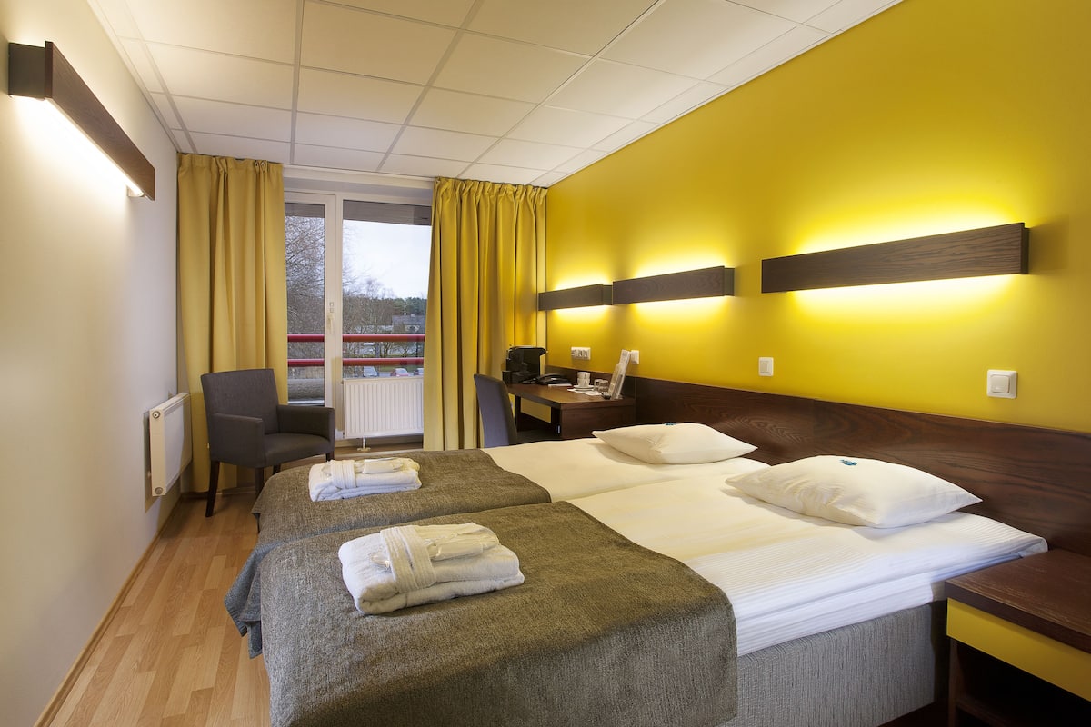 Une chambre d’hôtel avec deux lits, un bureau, une chaise et une fenêtre avec des rideaux.
