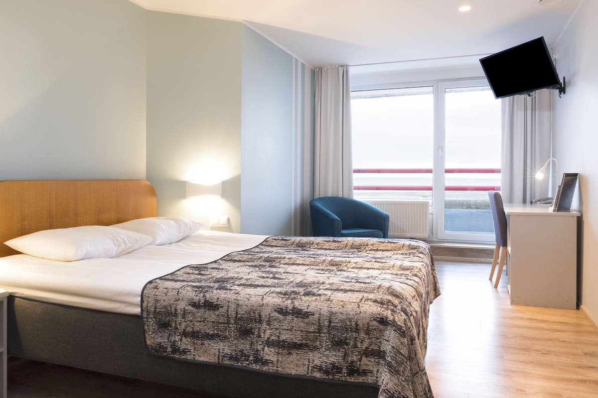 Une chambre d’hôtel équipée d’un lit, d’une table de chevet, d’une chaise, d’un bureau, d’une télévision et d’une grande fenêtre donnant sur un beau paysage.