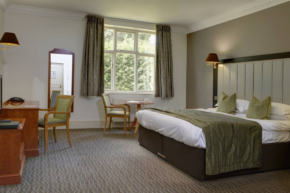 A hotel room with a bed, a desk, a chair, a small table, and a window with curtains.
