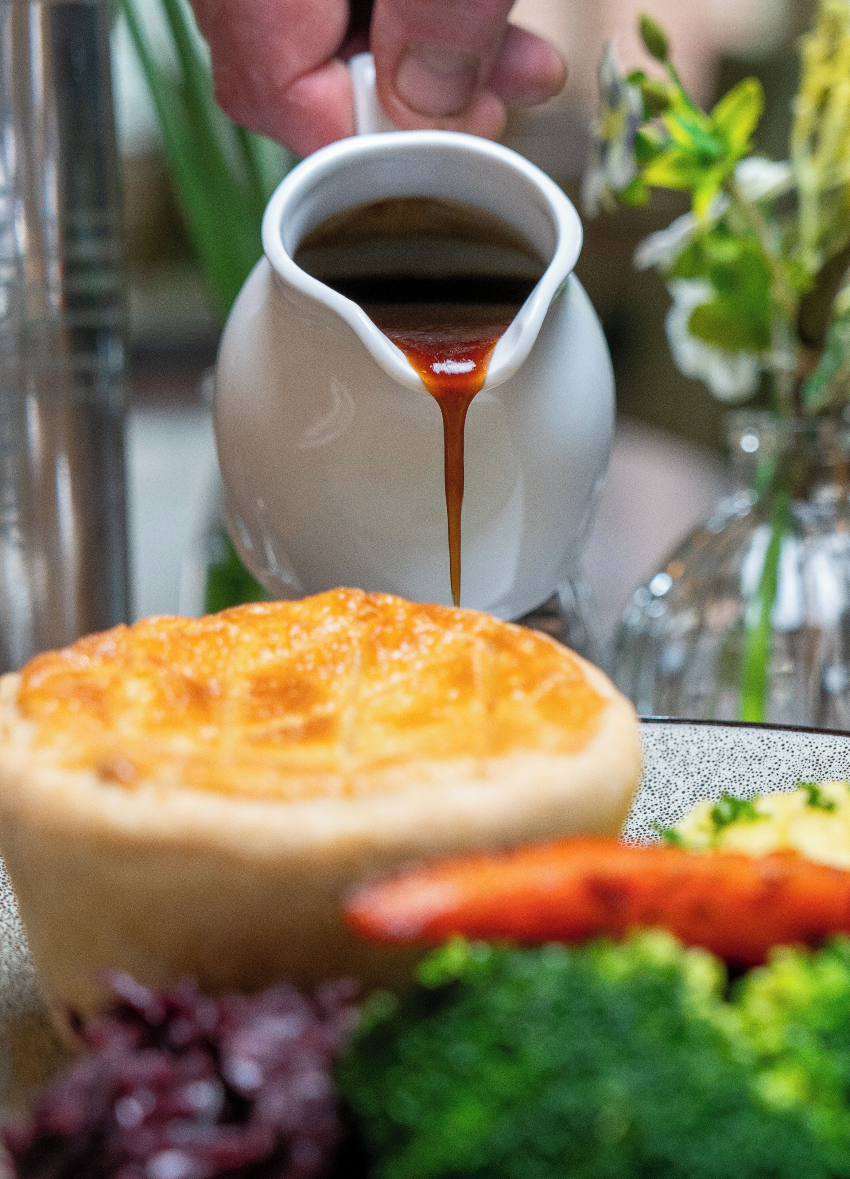 A close-up of a cup pouring a dark liquid, likely coffee, into a white ceramic cup.