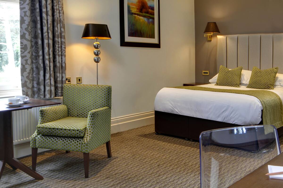 A hotel room with a bed, a desk with a chair, a lamp, and a painting on the wall.