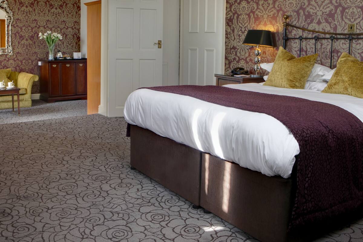 A bedroom with a large bed, a nightstand, a lamp, and a dresser.