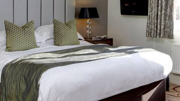 A neatly made bed with a patterned throw, a bedside lamp, and a television mounted on the wall.