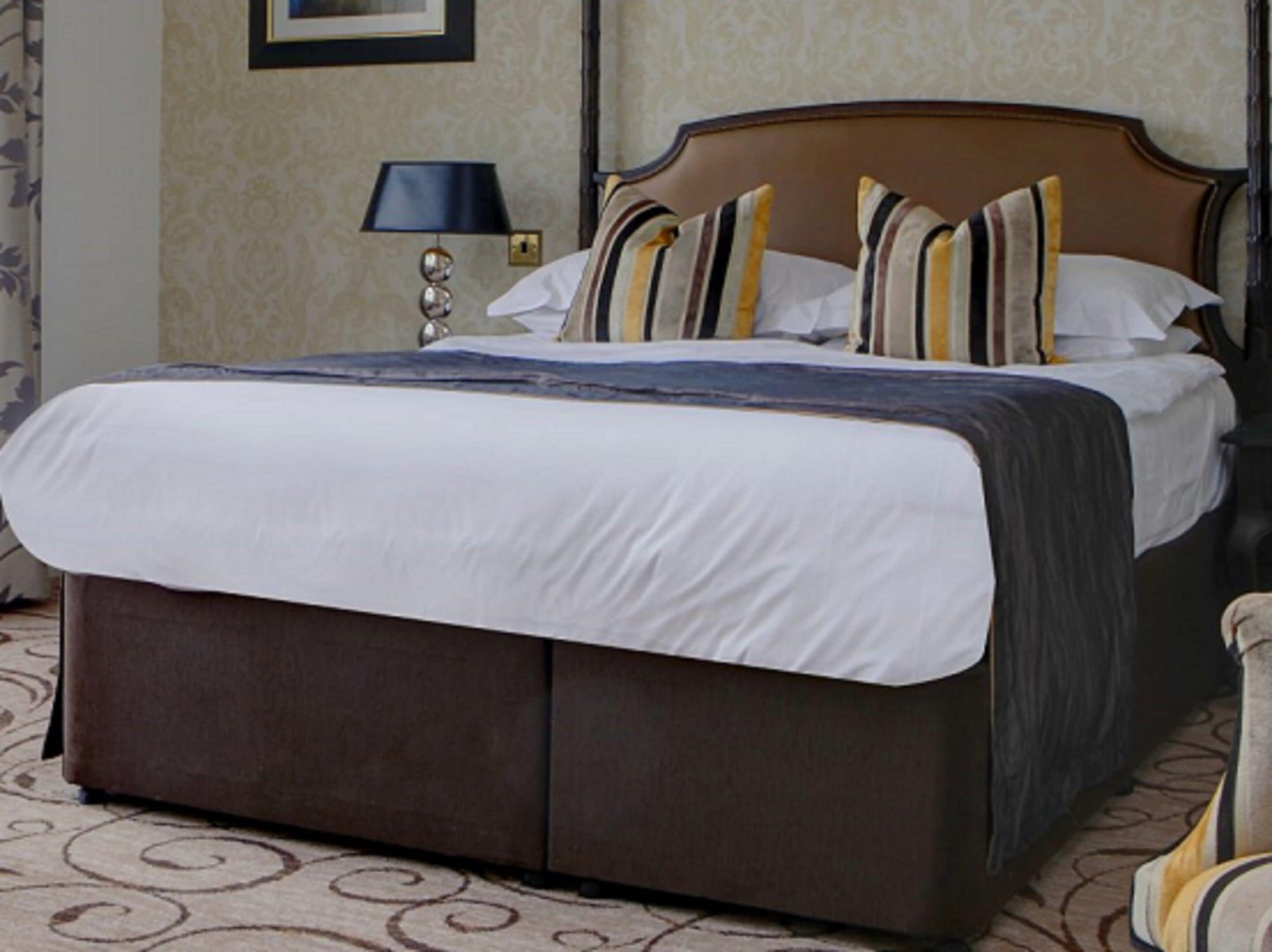 Una cama bien hecha con cabecera marrón, ropa de cama blanca y almohadas a rayas.