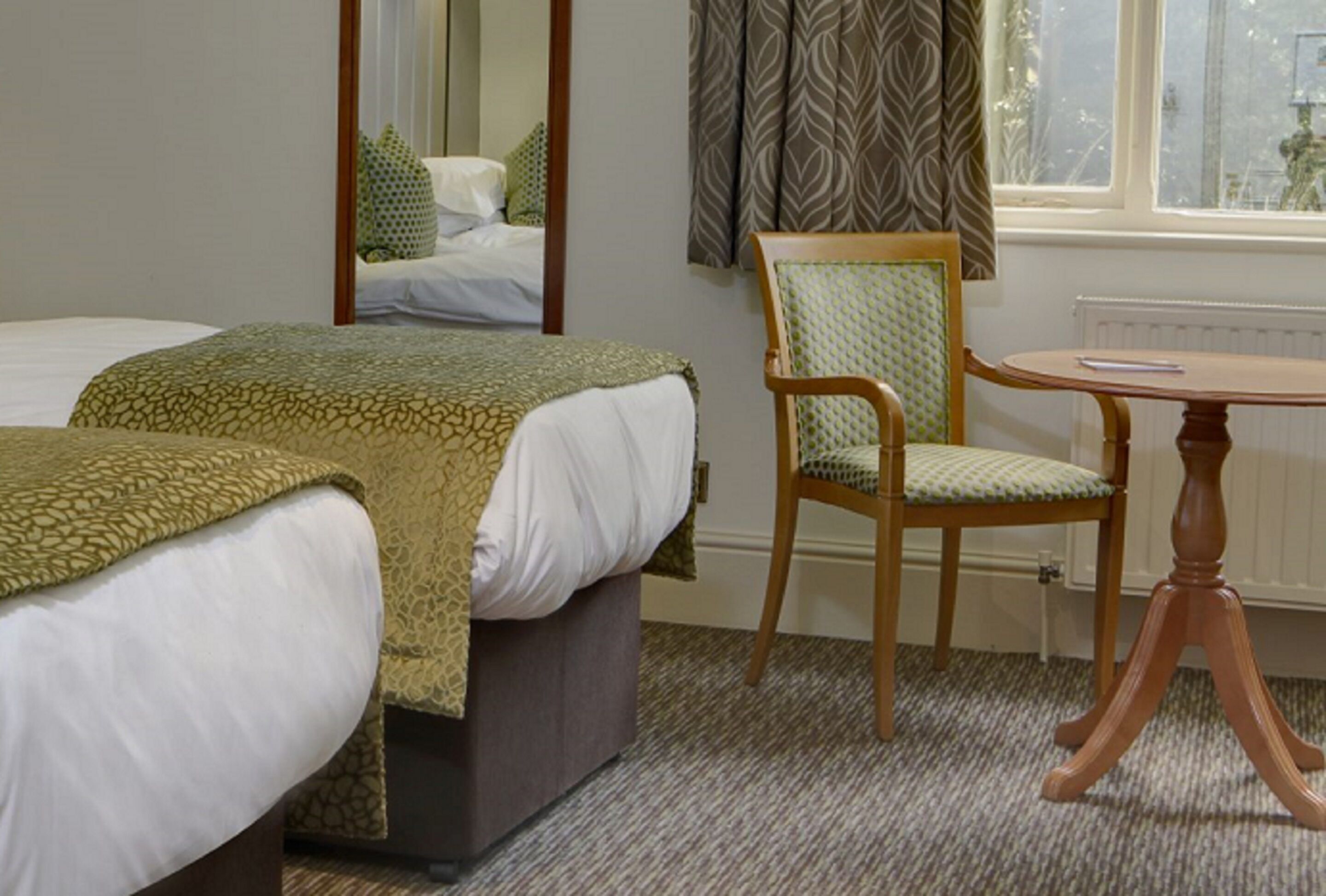 A hotel room with two beds, a wooden chair, a round table, and a window with curtains.