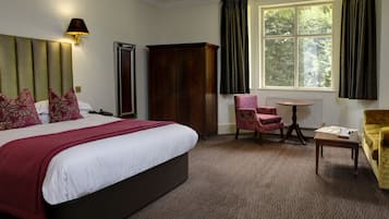 A hotel room with a large bed, a wardrobe, a chair, a small table, and a window with curtains.
