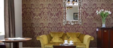 A room with a patterned wallpaper, a sofa, a table with a cup and saucer, and a cabinet.