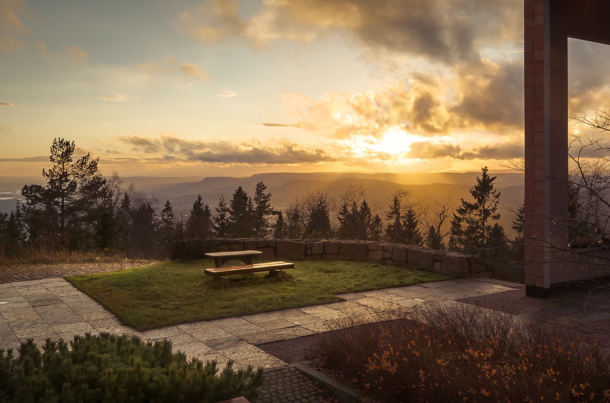 Un patio con un banco que ofrece vistas panorámicas de montañas y un atardecer.