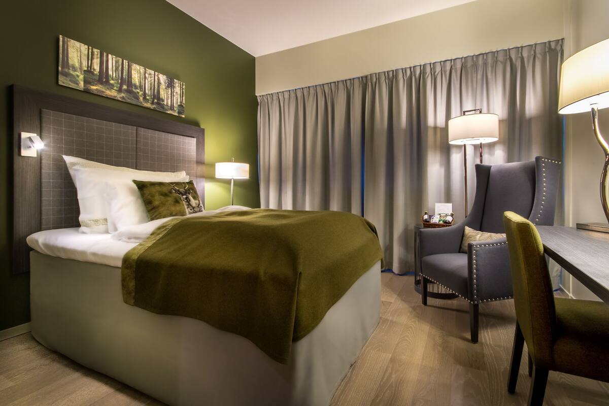 Et hotelværelse med en seng, et skrivebord, en stol og en lampe.