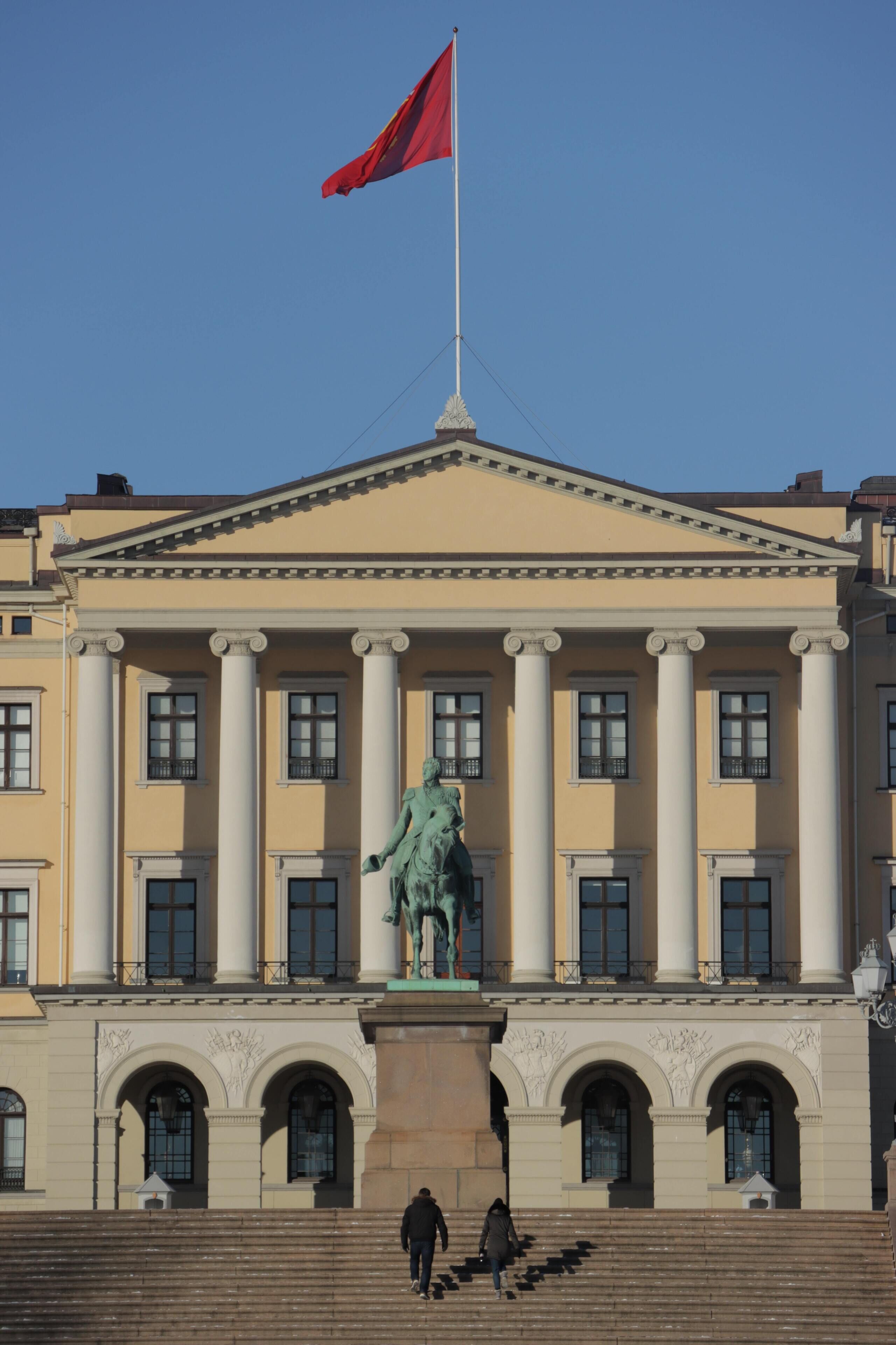 Un edificio de arquitectura clásica, con una estatua central, columnas y una bandera.