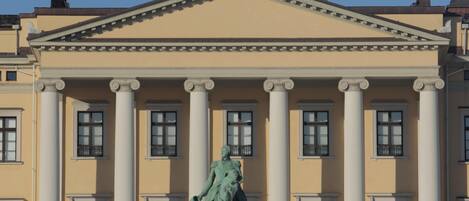 Un edificio de arquitectura clásica, con una estatua central, columnas y una bandera.