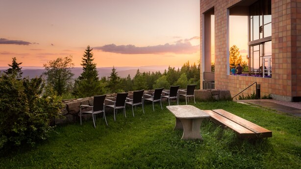 Un espacio al aire libre con sillas y una mesa, con vistas a un paisaje escénico de árboles y un horizonte lejano.