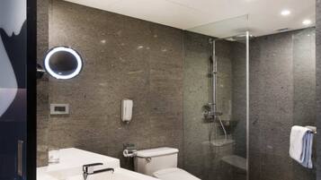 A modern bathroom with a glass-enclosed shower, a round mirror, and a white sink.