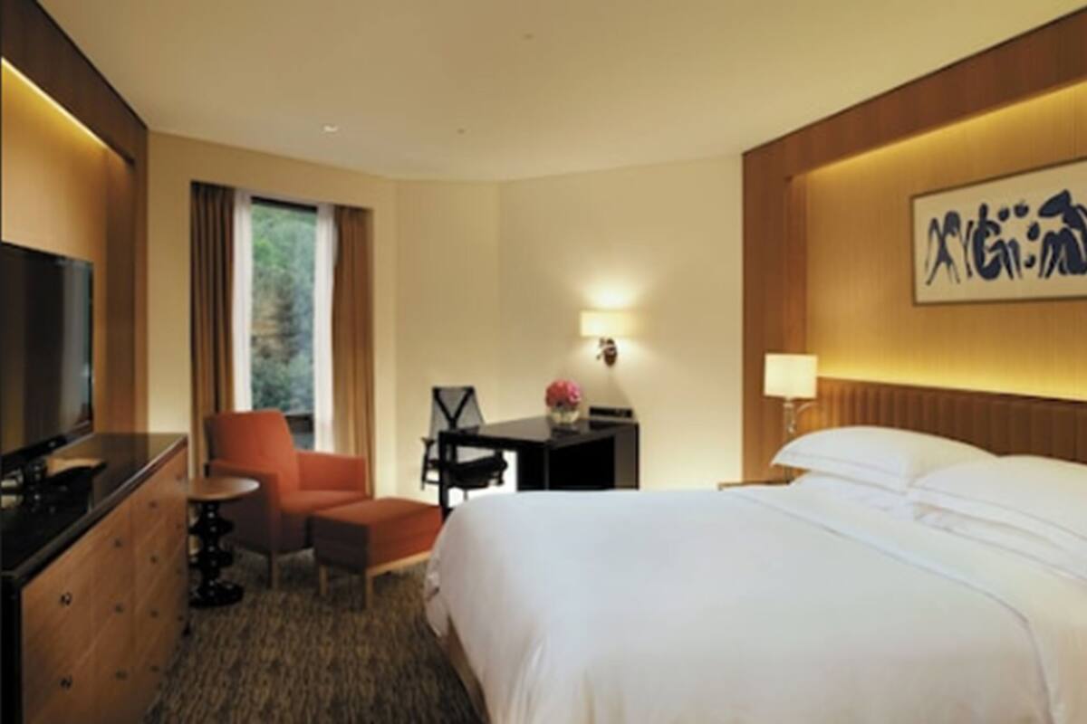 A hotel room with a bed, a desk, a chair, a TV, and a window with curtains.