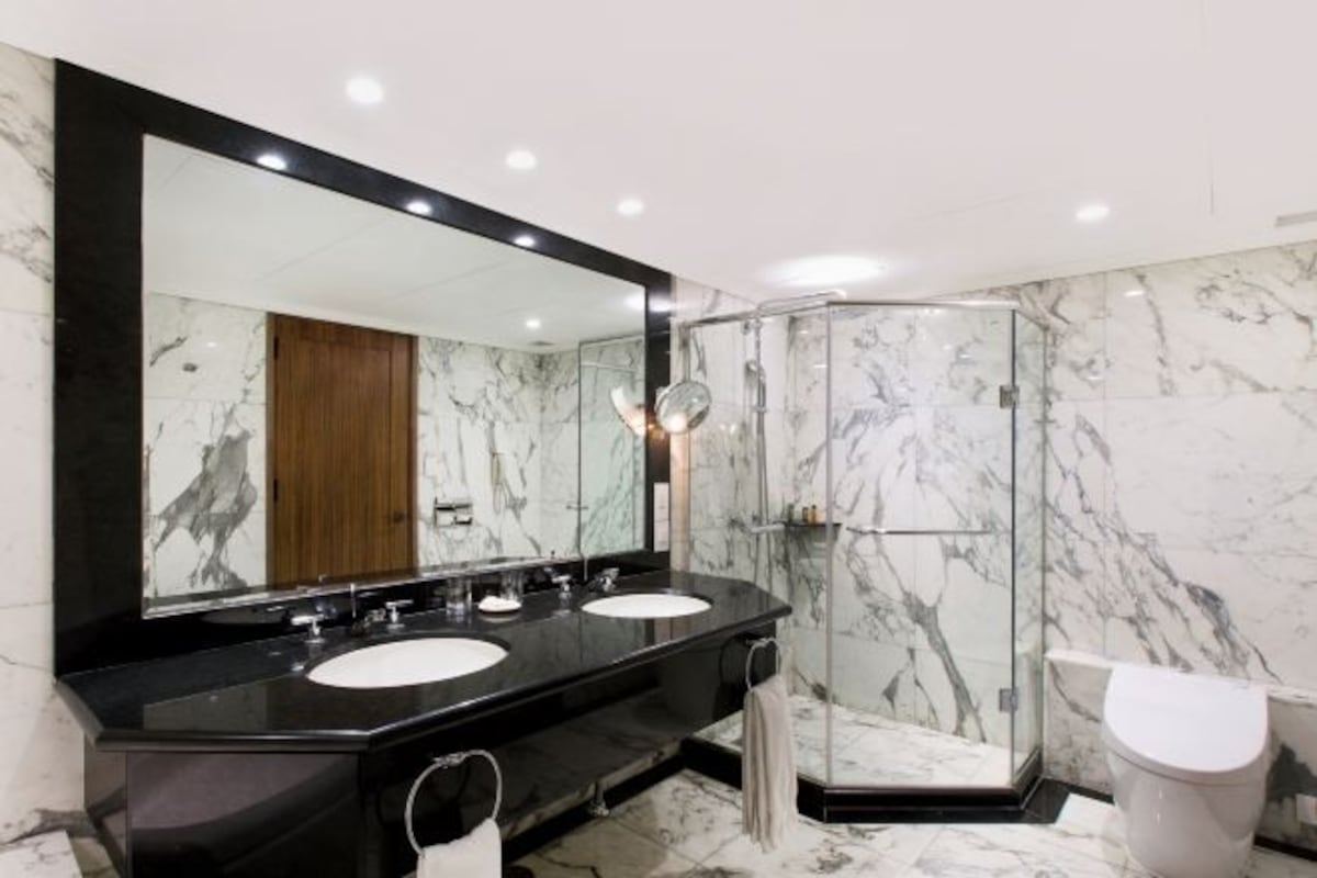 A modern bathroom with two sinks, a large mirror, a glass shower enclosure, and a toilet.