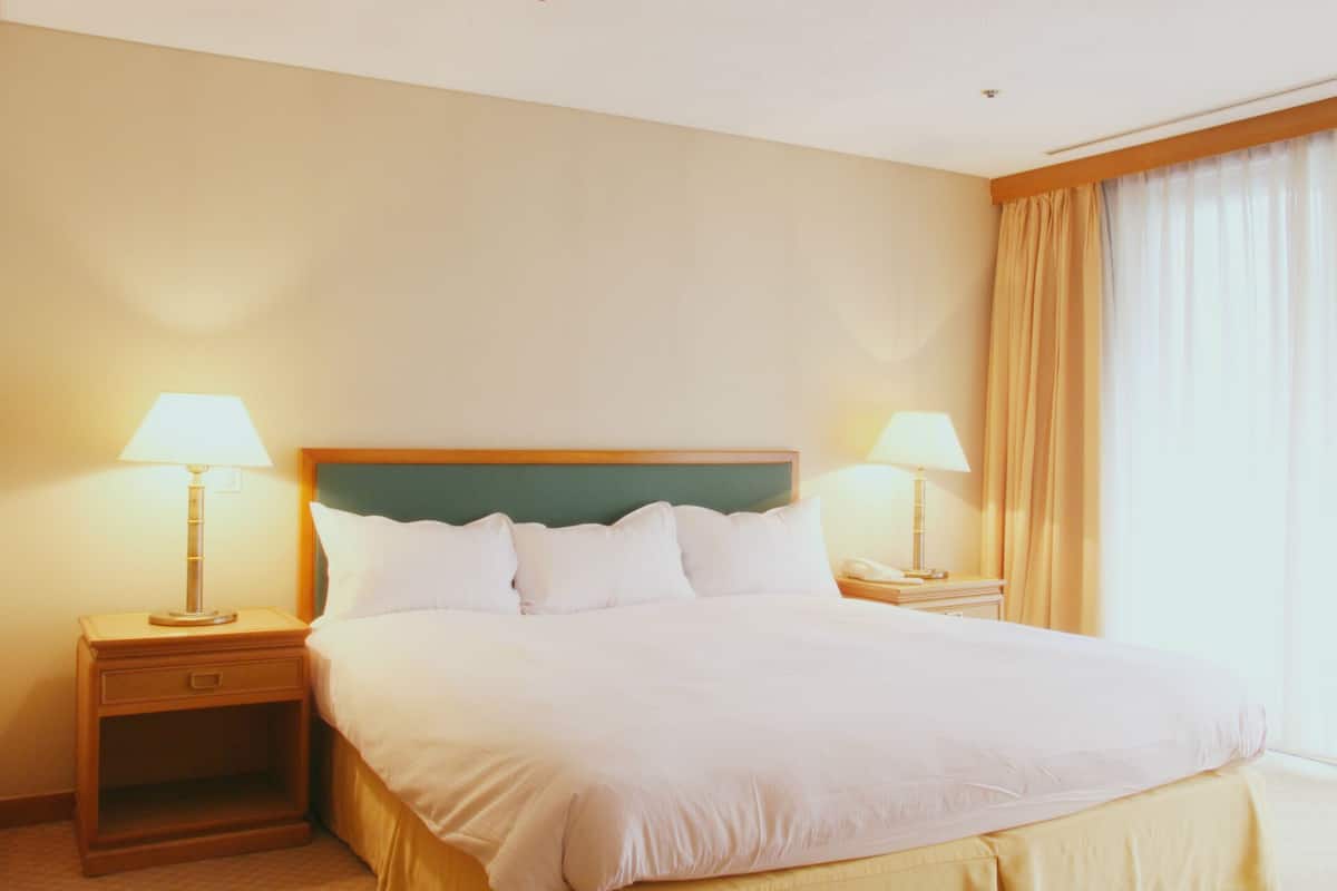 A hotel room with a large bed, two bedside tables with lamps, a wooden headboard, and a window with curtains.