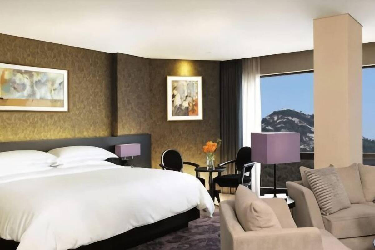 A hotel room with a large bed, a sofa, a small table with a lamp, and a view of mountains.