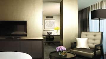 A hotel room with a bed, a TV, a desk with a chair, a sofa, a lamp, and a vase with flowers.