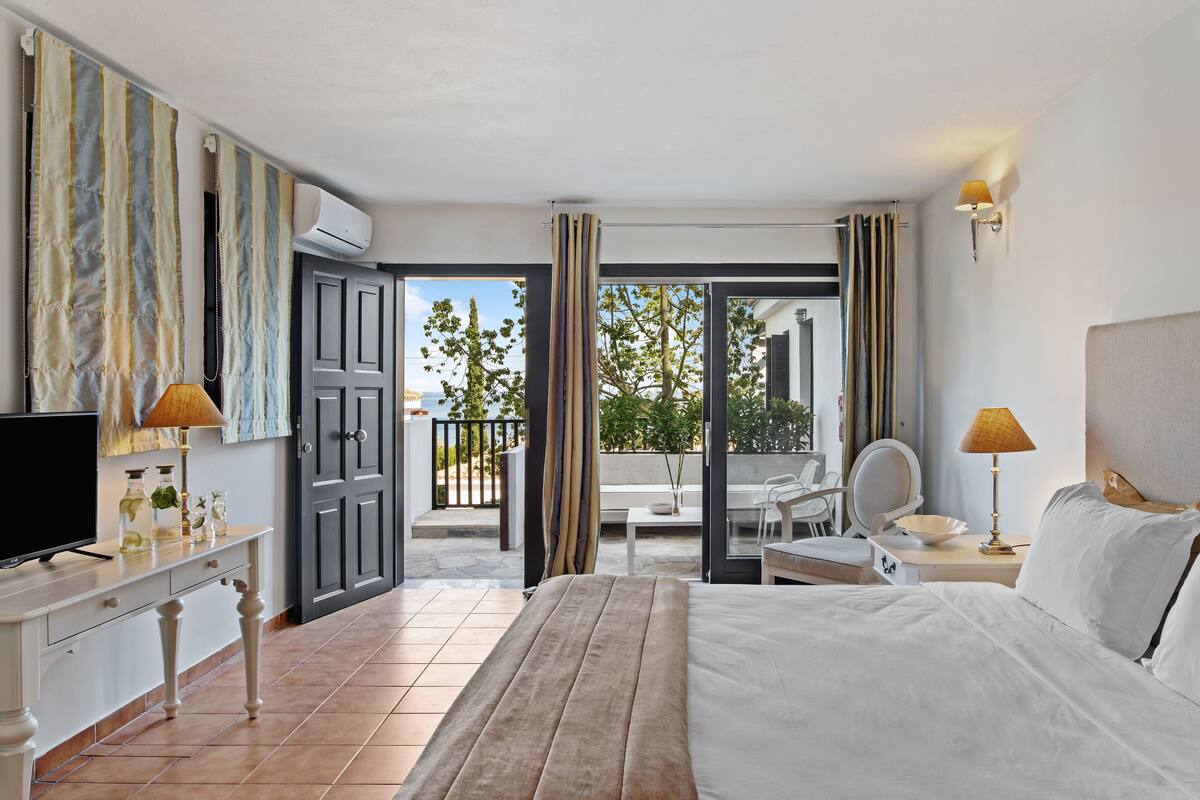 Una habitación de hotel con cama, escritorio con televisor, mesa con lámpara y balcón con silla y mesa.