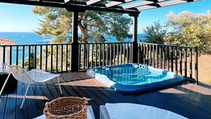 A covered outdoor seating area with a hot tub, lounge chairs, and a view of the sea.