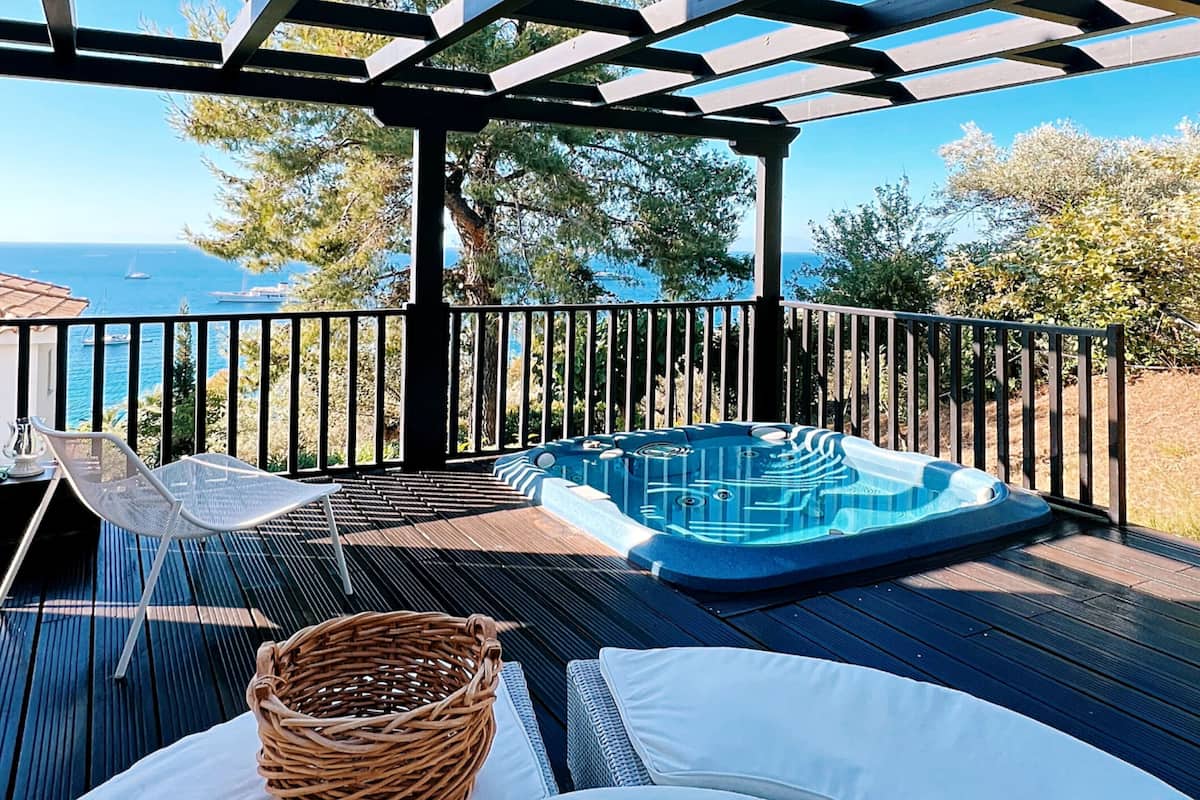 Un espacio de estar techado al aire libre con un jacuzzi, sillas de descanso y vistas al mar.