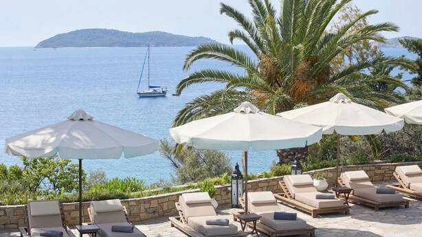 A poolside area with lounge chairs and umbrellas, overlooking a body of water with a sailboat.