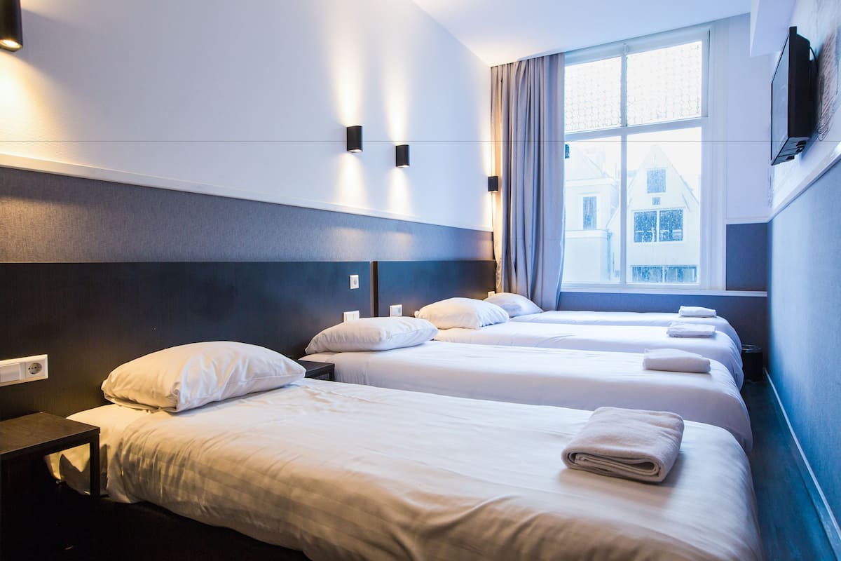 Habitación de hotel con tres camas, un televisor montado en la pared y una ventana con cortinas.