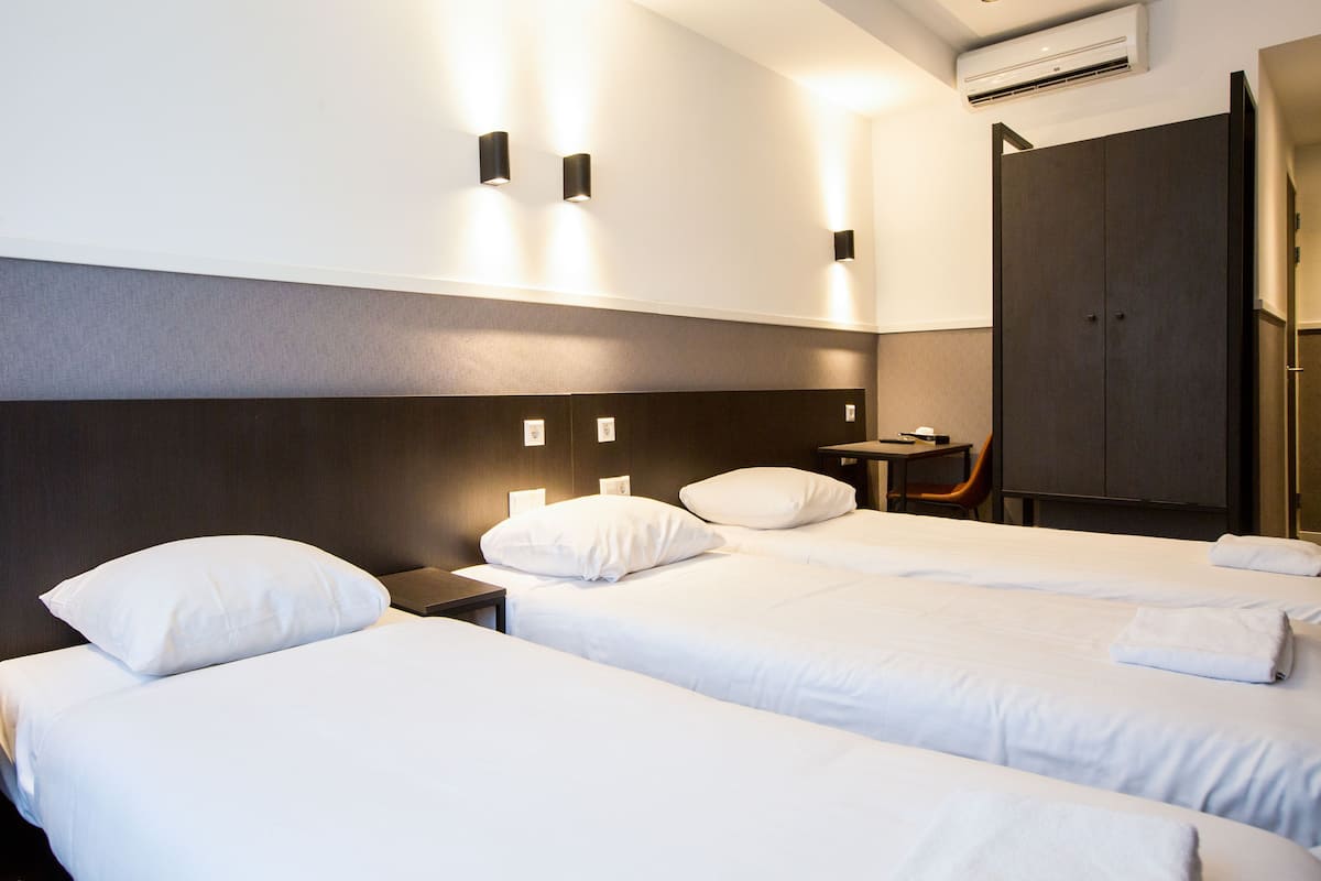 Una habitación de hotel con dos camas individuales, una mesita pequeña, una silla y un armario.