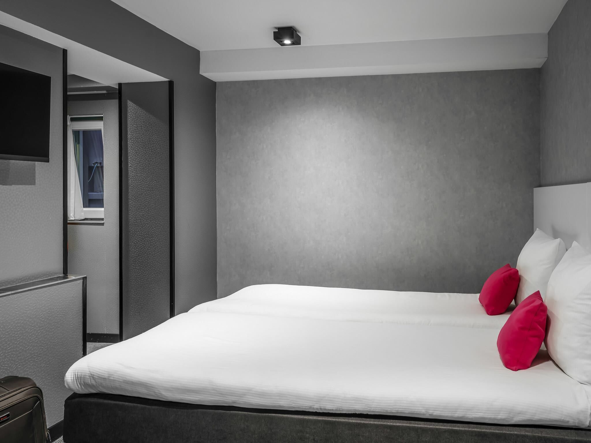 A modern hotel room with a large bed, a flat-screen TV, and a view of the outside.