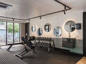 A gym with exercise equipment, mirrors, and a window with a view of bicycles. - ibis Styles Amsterdam Amstel (Amsterdam)